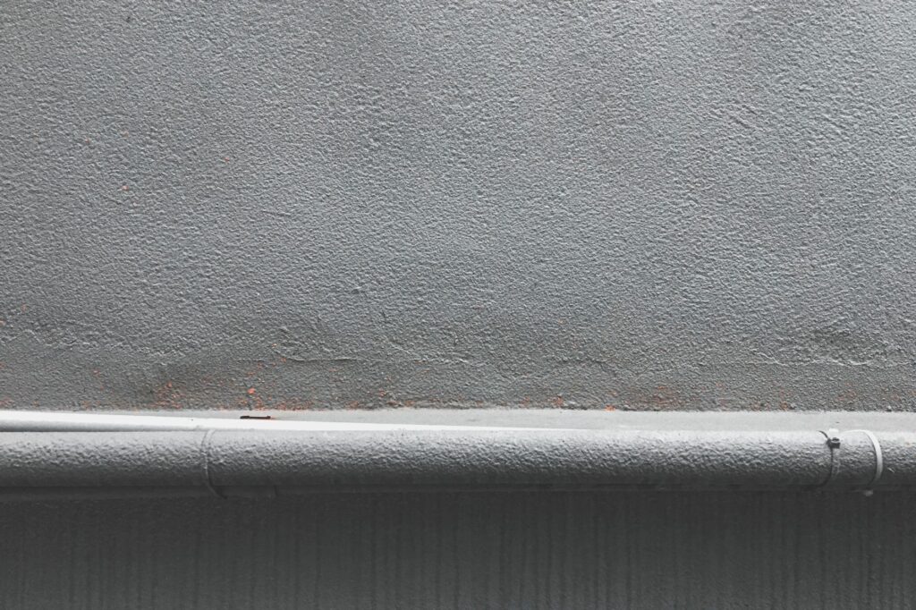 Close-up of a textured grey concrete wall with a metal pipeline along the bottom edge.