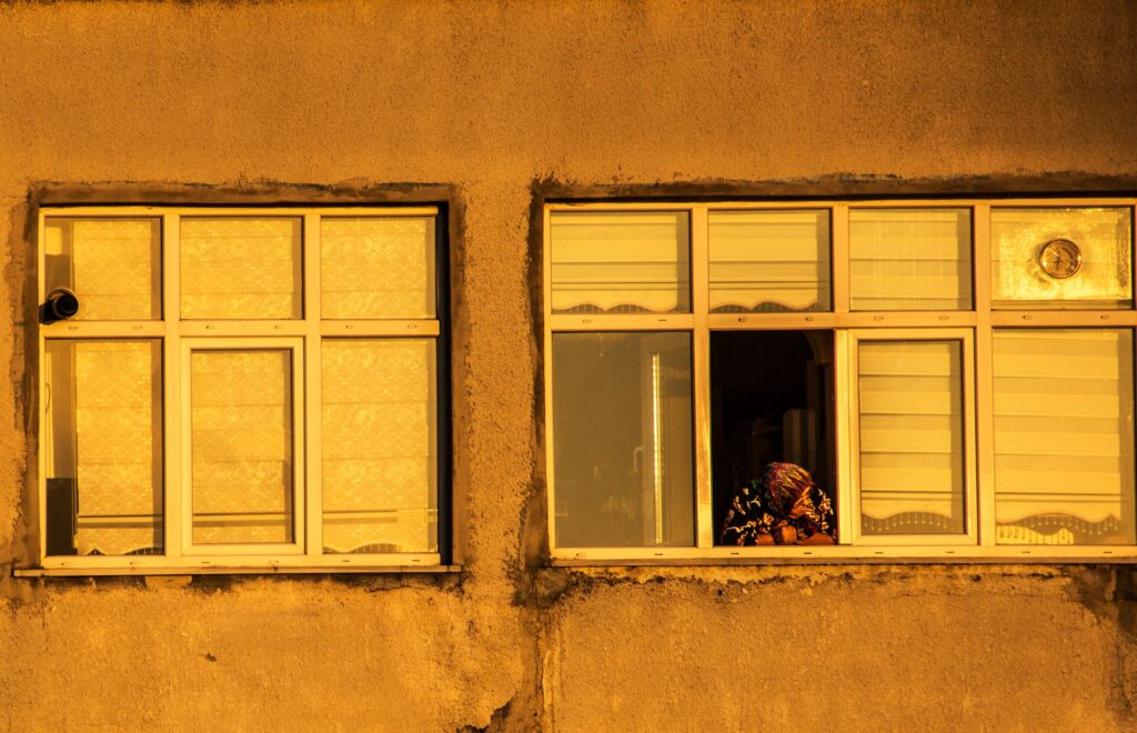 A solitary person gazes from a window, bathed in warm evening hues.