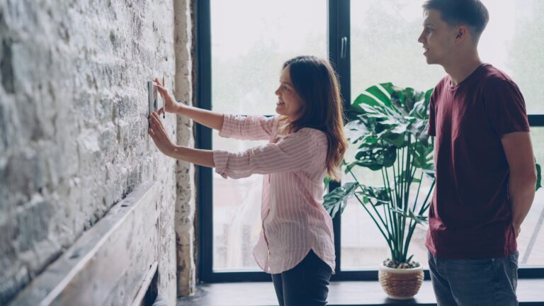 Young couple hanging a picture on a brick wall in a bright, modern living room.